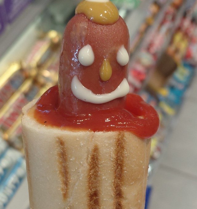 A creative dessert designed to look like a character, featuring a cake slice as the base, ketchup as the face, marshmallow details for eyes and a smile, and mustard accents on top.