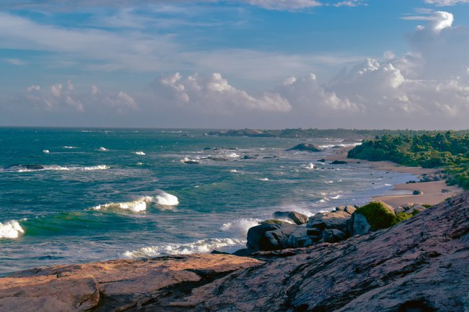 A picturesque rocky coastline stretches into the distance with turquoise waves rolling onto a sandy shore under a dramatic, cloud-filled sky, evoking a sense of serenity and renewal—fittingly mirroring the artistic theme of "Breathing Again." No text, numbers, tickers, or names are visible within the image itself.