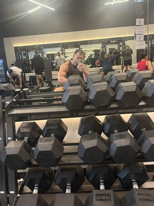 A muscular gym-goer captures a mirror selfie while flexing in the background, with a prominent dumbbell rack in the foreground labeled "CSE" — fitting the "Gains only" theme as the "CSE" branding doubles as a cheeky nod to "gains."