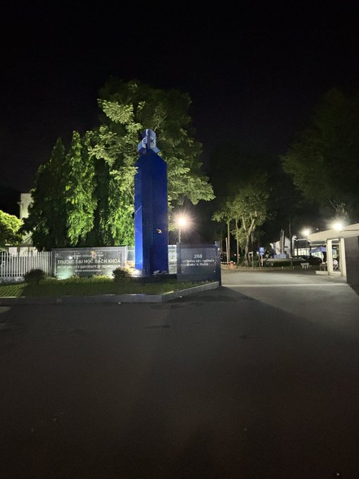 A nighttime photograph of a blue monument or memorial at an entrance, with the sign 'STUDENT'S DAY HOC LUEN NICA' and the number '268' visible on the front wall.