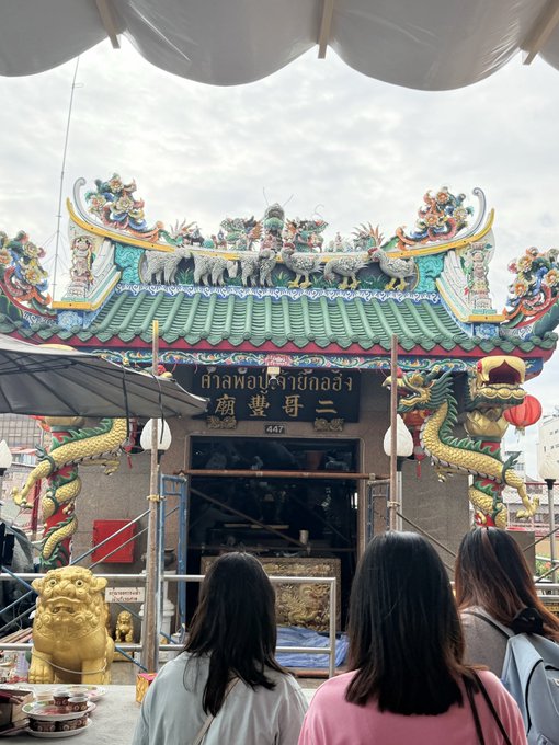 Three women stand before an ornate Chinese temple with dragon decorations, displaying Thai and Chinese characters including '二府王爺廟' and the address '447'.