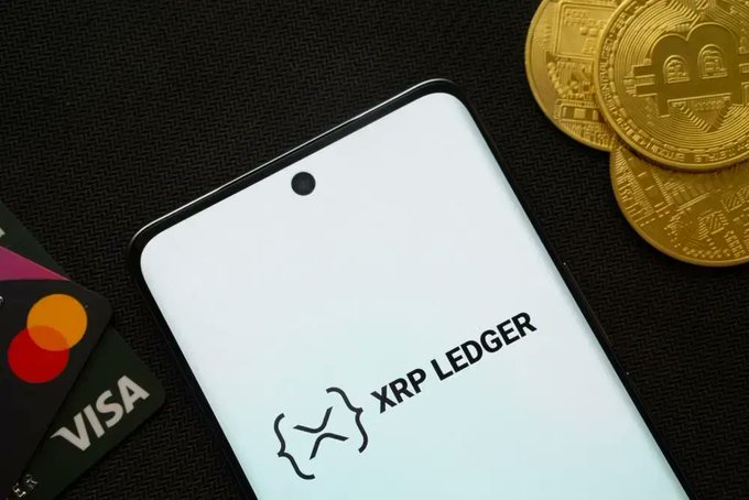 A smartphone displaying the "XRP LEDGER" logo sits on a dark surface alongside gold XRP-branded coins and credit cards (Mastercard and Visa), visually reinforcing the post's message of growing XRP adoption and expanding institutional and retail use cases.