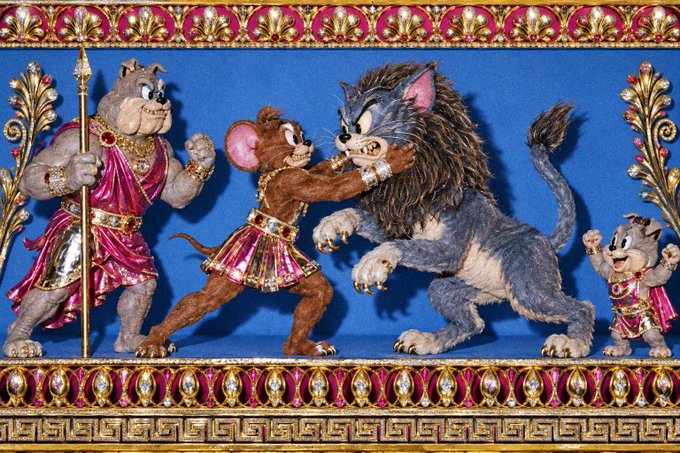 An ornate relief sculpture framed in gold and jeweled borders depicts a battle scene with two bulldog-like warriors in Roman-style armor facing a large gray cat monster and a smaller cat warrior.