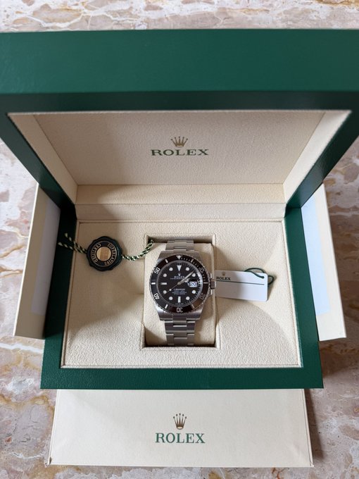 A Rolex Submariner Date watch with a black dial and bezel is displayed in its green Rolex presentation box, accompanied by the original hangtag and warranty booklet.

The image ties to the post's theme of achieving a lifelong dream—the author celebrates purchasing a Rolex, a coveted childhood goal, as a tangible reward for their success in the crypto trading journey.