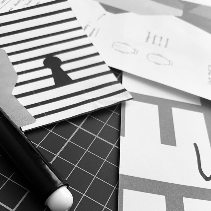 A black-and-white overhead shot shows design sketches, including a striped paper with a keyhole motif and a card with mirrored text reading "12E" and "214," alongside a pen on a grid cutting mat—visually echoing the post's hint at an in-progress creative project.