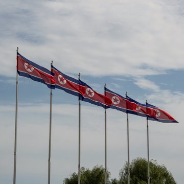 Five North Korean flags wave against a partly cloudy sky, visually representing the country's origin of the WaterPlum group accused of stealing $10.7 million in cryptocurrency through fake job recruiter schemes targeting over 30,000 devices in more than 100 countries.