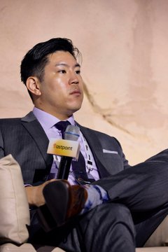 A man in a gray suit and purple tie holds a Bloomberg-branded microphone during what appears to be an interview or panel discussion.