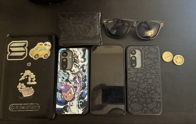 An overhead view shows everyday carry items on a dark surface, including a black bifold wallet with pins, two phone cases, sunglasses, a patterned fabric pouch, and two coins.
