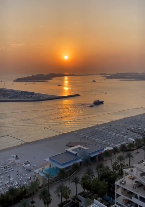 A breathtaking aerial sunset view over a beach resort, with the golden sun reflecting across calm waters and boats gliding near the shore. The serene coastal scene perfectly complements the post's message about staying focused and enjoying a beautiful day.