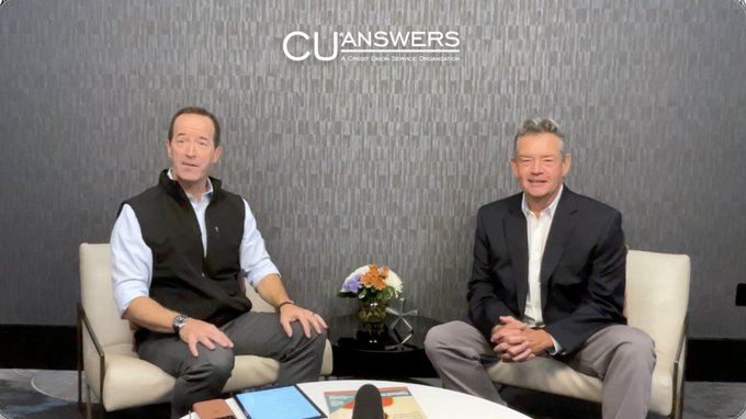 The image shows two men sitting across from each other in chairs, with a table between them. They appear to be engaged in an interview or discussion, as indicated by the presence of a microphone and a book nearby. The background features a gray wall, which complements the overall color scheme of the scene. The post that accompanies this image is titled "CU Answers" and provides information about a leadership conference taking place in 2016. It highlights key takeaways from the event related to stablecoins, AI, and agentic commerce, suggesting that these topics are at the forefront of banking innovation during that time period.