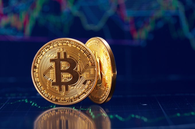 Two physical Bitcoin tokens rest against a blurred background of a green and red financial chart, highlighting cryptocurrency market themes.