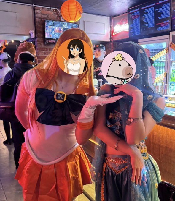 Two people pose indoors in colorful costumes, with their faces covered by cartoon avatar stickers, including an anime-style face and a small white character.