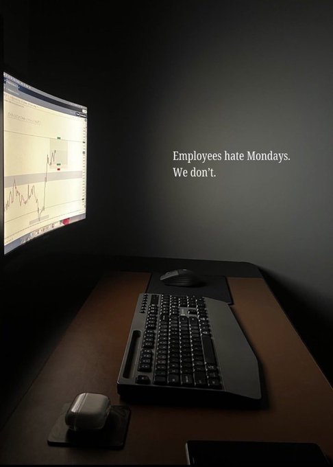 A dimly lit desk setup features a curved monitor displaying a stock chart, a mechanical keyboard, and a mouse, with the text 'Employees hate Mondays. We don't.' overlaid on the wall.