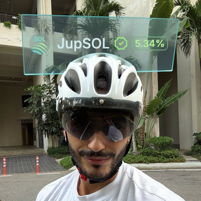 A man wearing a white cycling helmet and reflective sunglasses takes a selfie outdoors near a building with tropical plants. An augmented reality overlay displays "SOL", "JupSOL", a verified checkmark, and "5.34%" in a futuristic interface.
