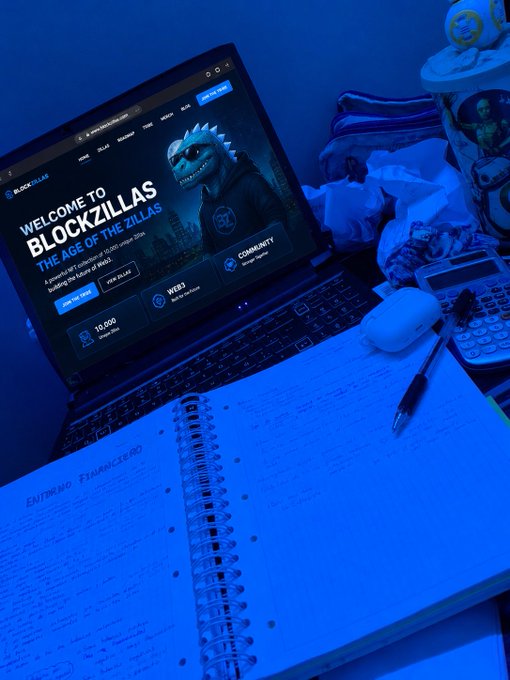 A blue-lit workspace featuring a laptop displaying 'Welcome to BlockZillas - The Age of the Zillas', alongside a spiral notebook with handwritten notes and a computer mouse.