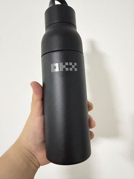 A hand holding a matte black water bottle with a pixelated white logo that appears to read 'IHX' or similar.