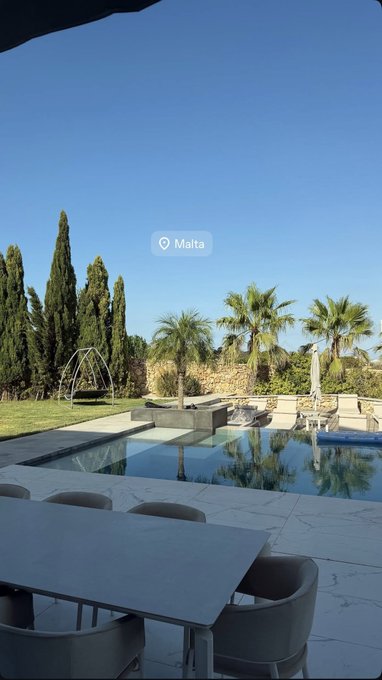 A serene outdoor poolside scene in Malta, featuring a marble dining table, modern chairs, palm trees, and a clear blue sky — the perfect morning coffee spot before diving into the CardCon weekend. 🏖️☕