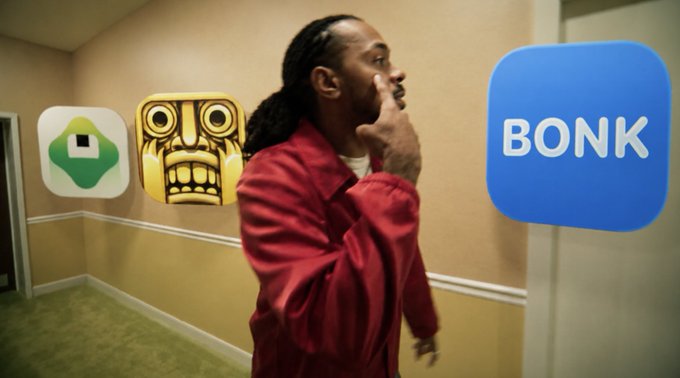 The image features a man wearing a red jacket, standing in an office hallway with a blue sign that says "BONK" above him. The man has his hand up to his mouth as if he's shouting or making a huge shoutout for someone named @tim_cook and @erickarcelliott who contributed to the post.