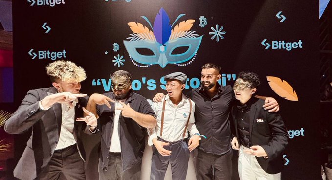 Five men in suits pose together in front of a "Bitget" branded backdrop featuring a Venetian-style mask and Bitcoin symbols, with text partially reading "Ven...to's...iti," capturing a celebratory VIP event moment that reflects the speaker's long-standing partnership and appreciation for Bitget's hospitality.
