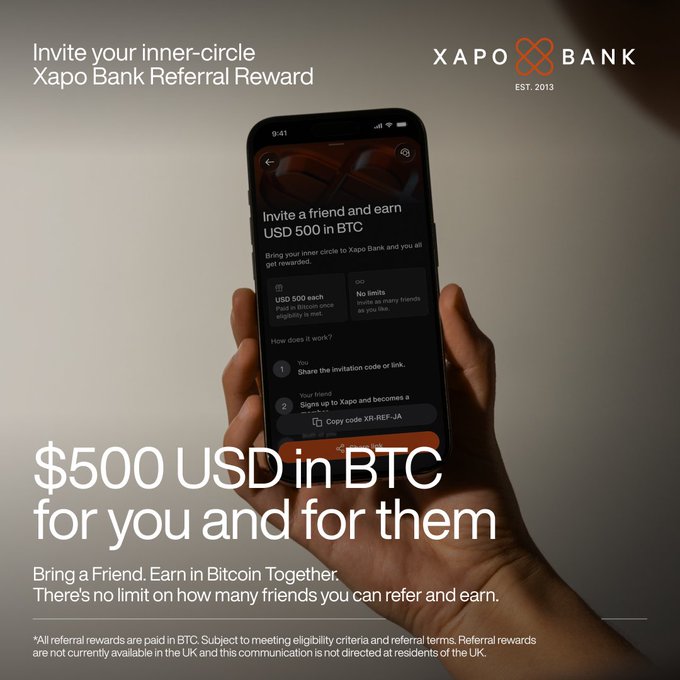 The image is a promotional ad for Xapo Bank's Referral Reward program, showing a hand holding a smartphone displaying the app's referral screen with the headline "Invite a friend and earn USD 500 in BTC" and copy reading "$500 USD in BTC for you and for them." The accompanying post relates by highlighting that referral rewards effectively cover half of a new member's first year, reinforcing the financial value of the promotion shown in the ad.