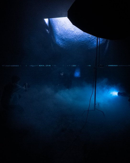 A dark, atmospheric scene from a film or video game shows a figure in a smoky environment illuminated by a bright blue light, with on-screen digital text visible.