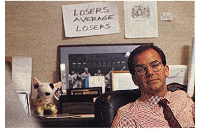 A man in glasses and a tie sits confidently at his desk beneath a handwritten sign reading "LOSERS AVERAGE LOSERS" — a pointed warning to those hesitant about adding long positions, suggesting hesitation will leave them "ngmi" while the bold thrive.