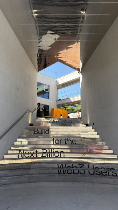 A modern architectural stairway features projected text reading 'BNB Chain Build for the Next Billion Web3 Users' on the steps leading upward.