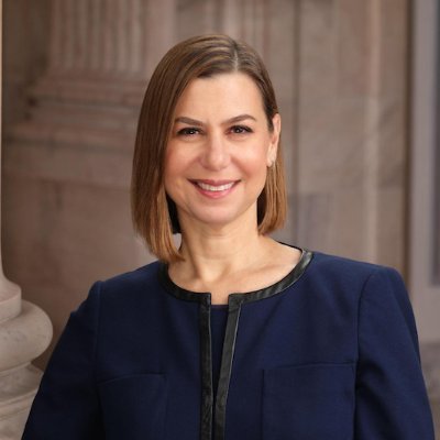 Senator Elissa Slotkin smiles while wearing a navy blue blazer with black trim, posed in what appears to be an official government building. The image accompanies news of her voting against advancing the CLARITY Act due to concerns about its ethics provisions.