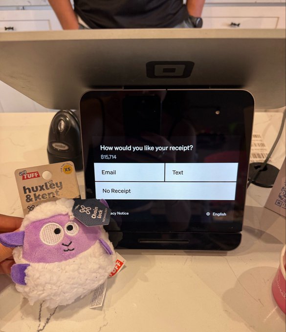 A plush "Huxley & Kent" dog toy sits next to a Square payment terminal displaying a receipt prompt with options for "Email," "Text," or "No Receipt" and an order subtotal of $157.14, illustrating a Bitcoin transaction at a Jersey Shore retailer as mentioned in the post.