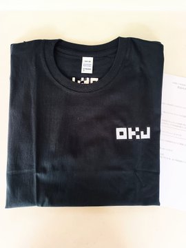 The image shows a black t-shirt with white text that reads "OKJ" and "stepn", as well as an accompanying paper. The t-shirt appears to be folded, possibly for storage or transport purposes. The presence of both the t-shirt and the paper suggests that they might be related in some way, such as a promotional item or a gift.