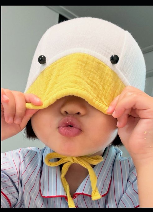 A child wearing a duck-themed fleece hat pulls the yellow beak over their eyes and puckers their lips playfully.