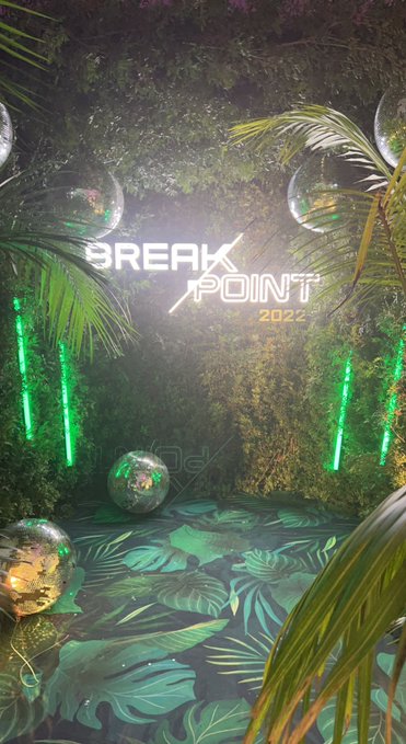 An atmospheric photo of a jungle-themed installation with neon green lights, disco balls, tropical plants, and a 'BREAK POINT 2022' sign.