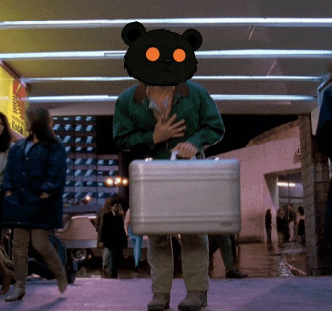 A still from a movie showing a person carrying a silver briefcase in what appears to be a store or mall, with their head replaced by a black cartoon bear face with glowing orange eyes.