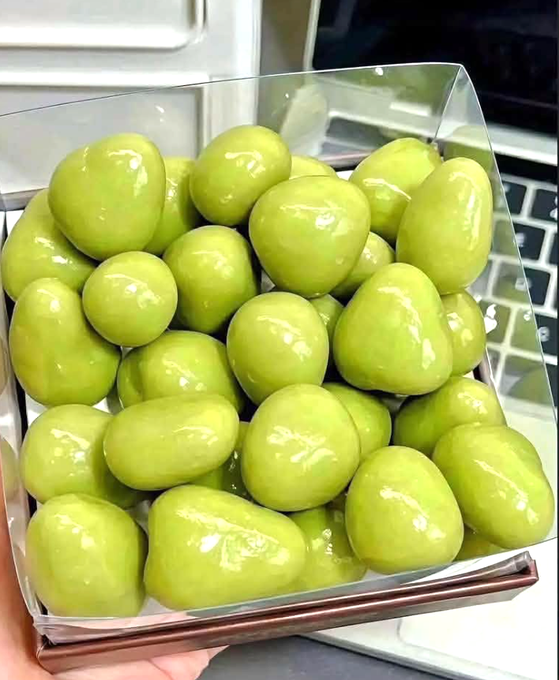 A box filled with glossy, plump green grapes being held over a laptop.