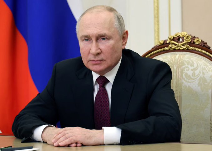 President Vladimir Putin sits at a desk in a formal setting, with the Russian flag behind him. The image underscores his authority as he signed Russia’s first cryptocurrency regulation law.