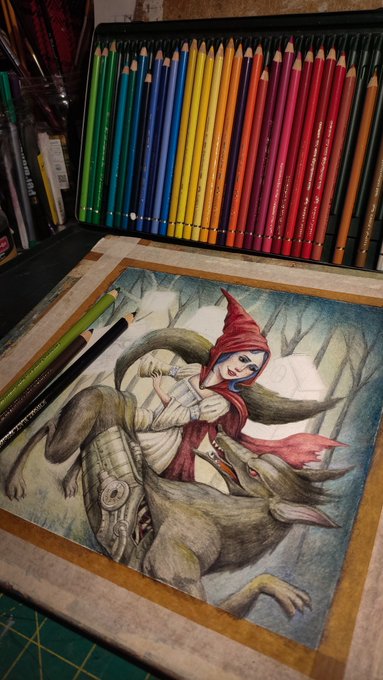 A completed colored pencil illustration depicting a hooded, red-cloaked character (resembling Little Red Riding Hood) holding a knife to a wolf's neck, displayed alongside a full set of arranged colored pencils.