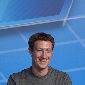 The image features a man wearing a gray t-shirt who appears to be smiling at the camera. The background of the photo shows a blue wall with white lines, which could potentially represent a grid or pattern. There are also some text elements visible in the image that read "LATEST: Meta has begun paying some creators in $USDC" and "focus on what is in the image and how it relates to the post." The man's smile suggests he might be discussing or promoting this new payment system, possibly related to the Metaverse.
