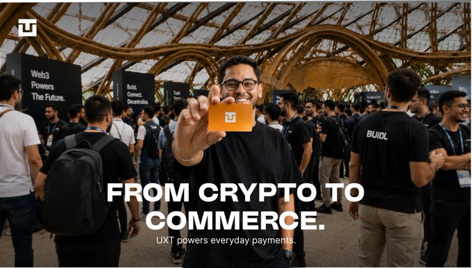 A man smiles while holding an orange UXT card at a tech event, with the text 'FROM CRYPTO TO COMMERCE. UXT powers everyday payments.' and signage reading 'Web3 Powers The Future' visible in the background.