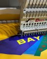 A row of Bored Ape Yacht Club (BAYC) branded burgee flags rests on a wooden surface, with the iconic blue flag featuring yellow "BAYC" lettering prominently displayed alongside an open notebook. The image relates to the post about a BAYC x Sean Wotherspoon burgee flag raffle, showing the actual flags being given away in the contest.