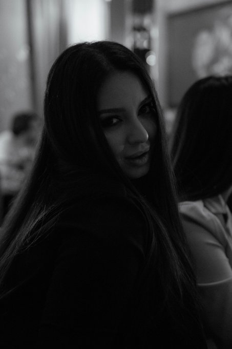 A black and white portrait photograph of a woman with long dark hair looking back over her shoulder.