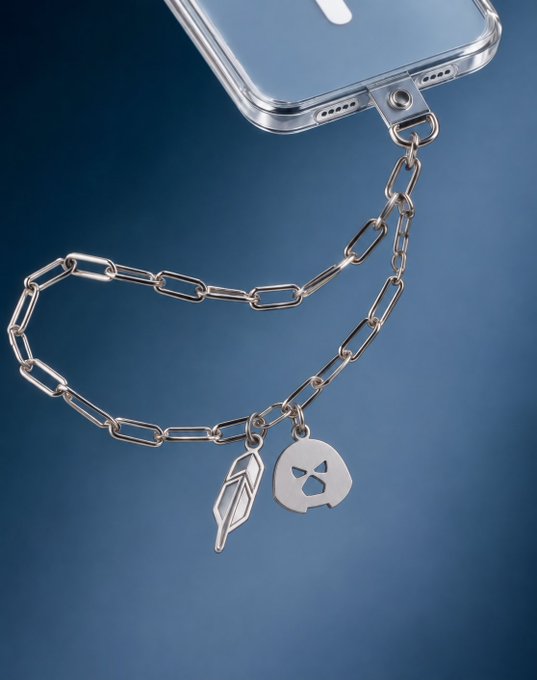 Silver paperclip-style chain phone charm with two pendants—a feather and a peace sign skull—attached to a clear phone case.