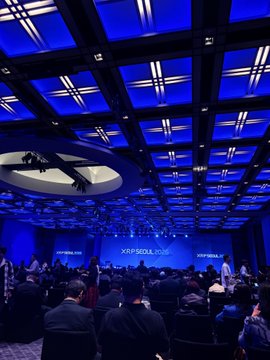 A conference hall with blue lighting and a panel on stage; the screens display 'CRYPTO SOCIAL 2024'.
