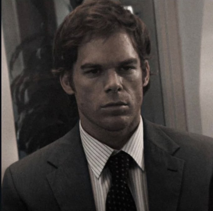 A man in a grey suit, striped shirt, and dotted tie stares blankly with a deadpan, unimpressed expression, perfectly capturing the skeptical reaction to someone's decision to abandon college for memecoins.