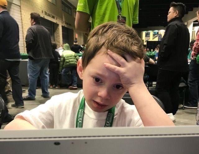 A young boy with a "FIRSTLOOK" lanyard appears frustrated, holding his head in his hand while looking at a screen, seemingly at an event where NFT whitelists and mints are being distributed—capturing the bewilderment expressed in the post about how everyone at @0xAlphaGEMs keeps securing NFT WL slots.