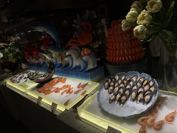 A lavish seafood display features a platter of mussels on ice alongside shrimp and fish, accompanied by a decorative boat centerpiece and white roses. The image accompanies a social media post about being generously treated by a chairman to an extravagant dining experience.