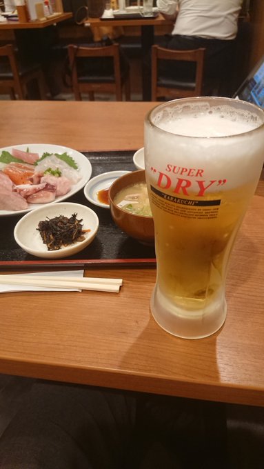 A Japanese meal setting with sashimi, miso soup, and a glass of Asahi Super Dry beer on a wooden table.