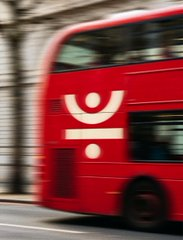 A red double-decker bus speeds by in a motion-blurred photograph, likely symbolizing a promotional campaign in motion. The accompanying text about TRON's DeFi Summer S2 campaign and its $2.35 million incentive budget suggests the image serves as a visual metaphor for the campaign's momentum and reach, akin to a bus rapidly mobilizing users toward deposits and liquidity.