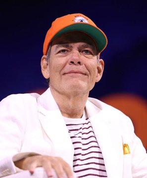 The image shows a man wearing an orange cap and white jacket over a striped shirt, smiling. This appears to be Max Keiser, the financial commentator referenced in the post, which discusses his warning about the U.S. debt crisis driving Bitcoin's price above $2,000,000.