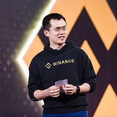 A man identified as CZ, CEO of Binance, stands on stage wearing a black hoodie with the Binance logo and text visible on it, appearing to give a presentation. The image relates to the post as it depicts the Binance executive whose prediction about Bitcoin potentially reaching $1 million much sooner than 25 years is being highlighted.