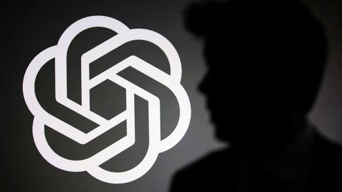 The silhouette of a man stands beside the illuminated OpenAI logo, visually accompanying news of CEO Sam Altman's hint at a potential pact among AI companies to address safety risks.
